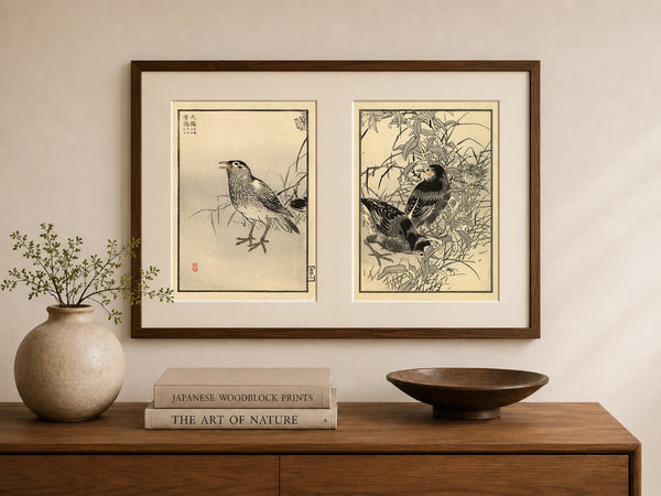 A framed pair of Japanese woodblock bird prints hanging on a beige wall above a wooden console table with a vase, books, and a bowl.